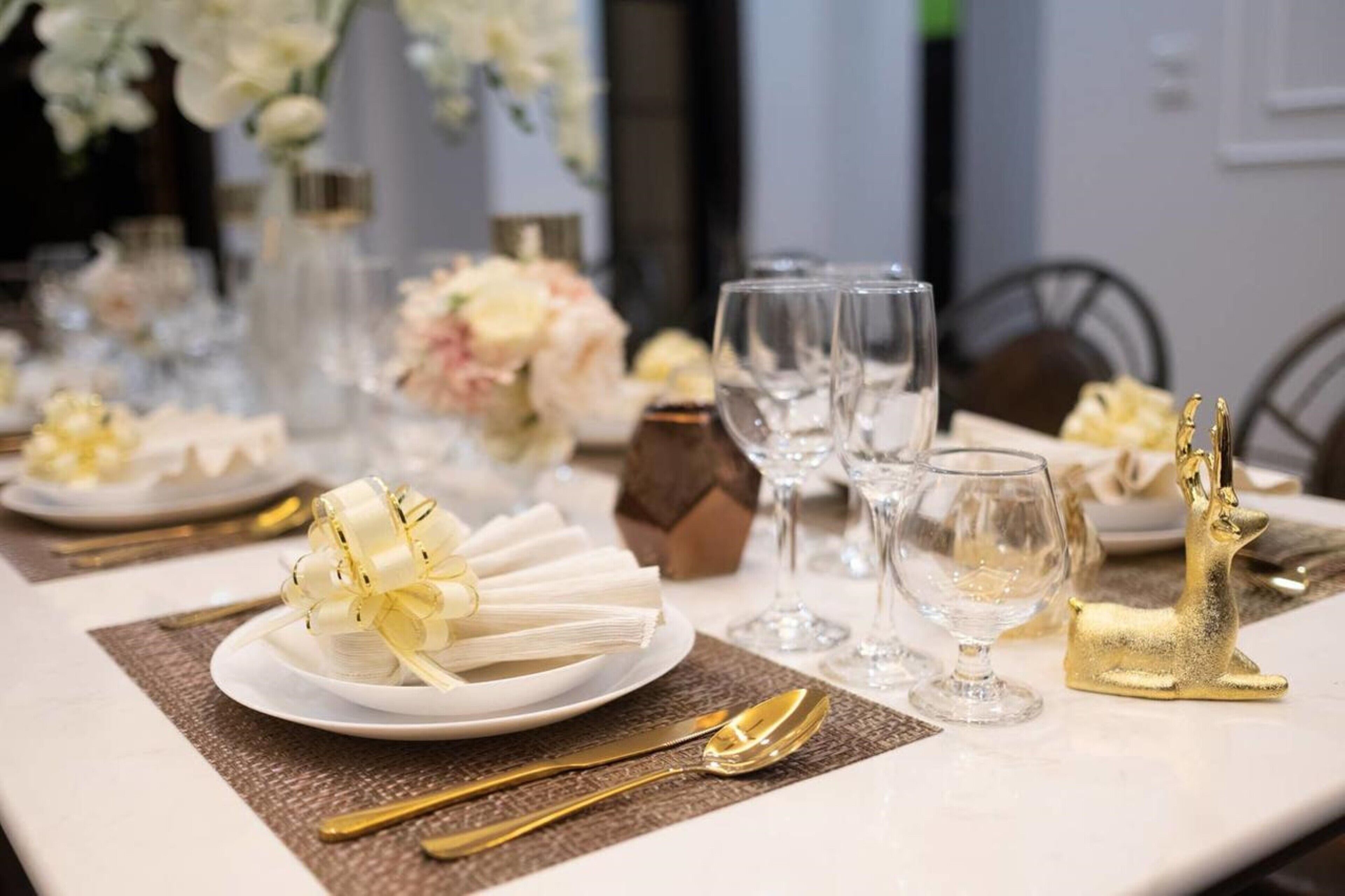 A table set for a formal dining occasion with white plates, gold cutlery, and clear glassware.
