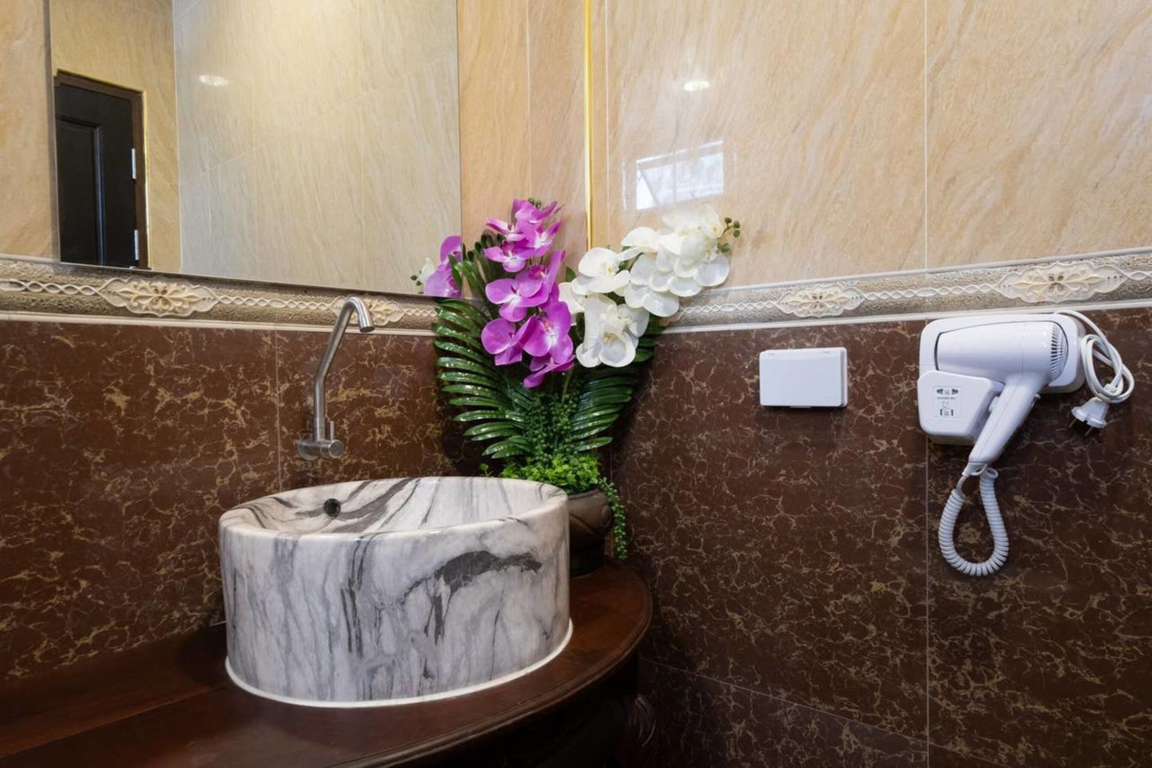 A marble sink, a hair dryer, and a vase with flowers in a bathroom.