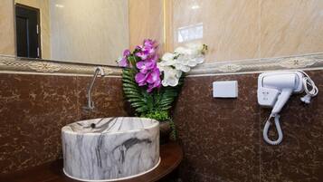 A marble sink, a hair dryer, and a vase with flowers in a bathroom.