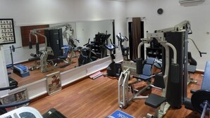 A gym with various exercise machines, a large mirror, and a wooden floor. - Terrace Green Hotels (Lagos)