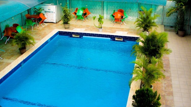 An indoor swimming pool with a tiled edge, surrounded by potted plants and colorful chairs. - Terrace Green Hotels (Lagos)