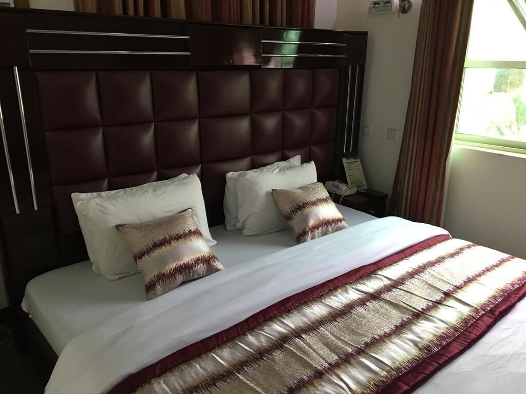 Ein Hotelzimmer mit einem großen Bett, einem gepolsterten Kopfteil und einem Fenster mit Vorhängen.