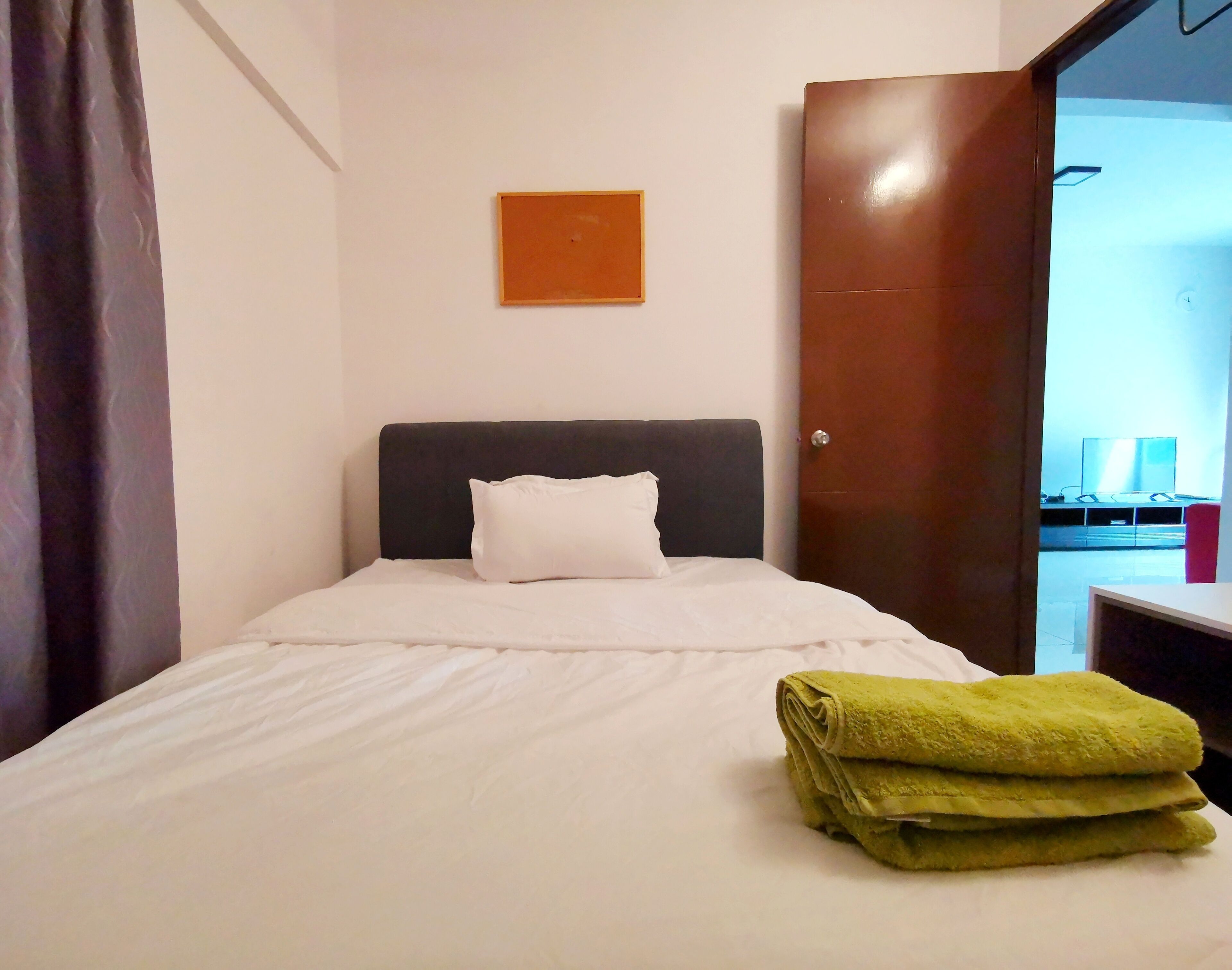 A neatly made bed with white bedding, a single white pillow, and a green towel on the side.