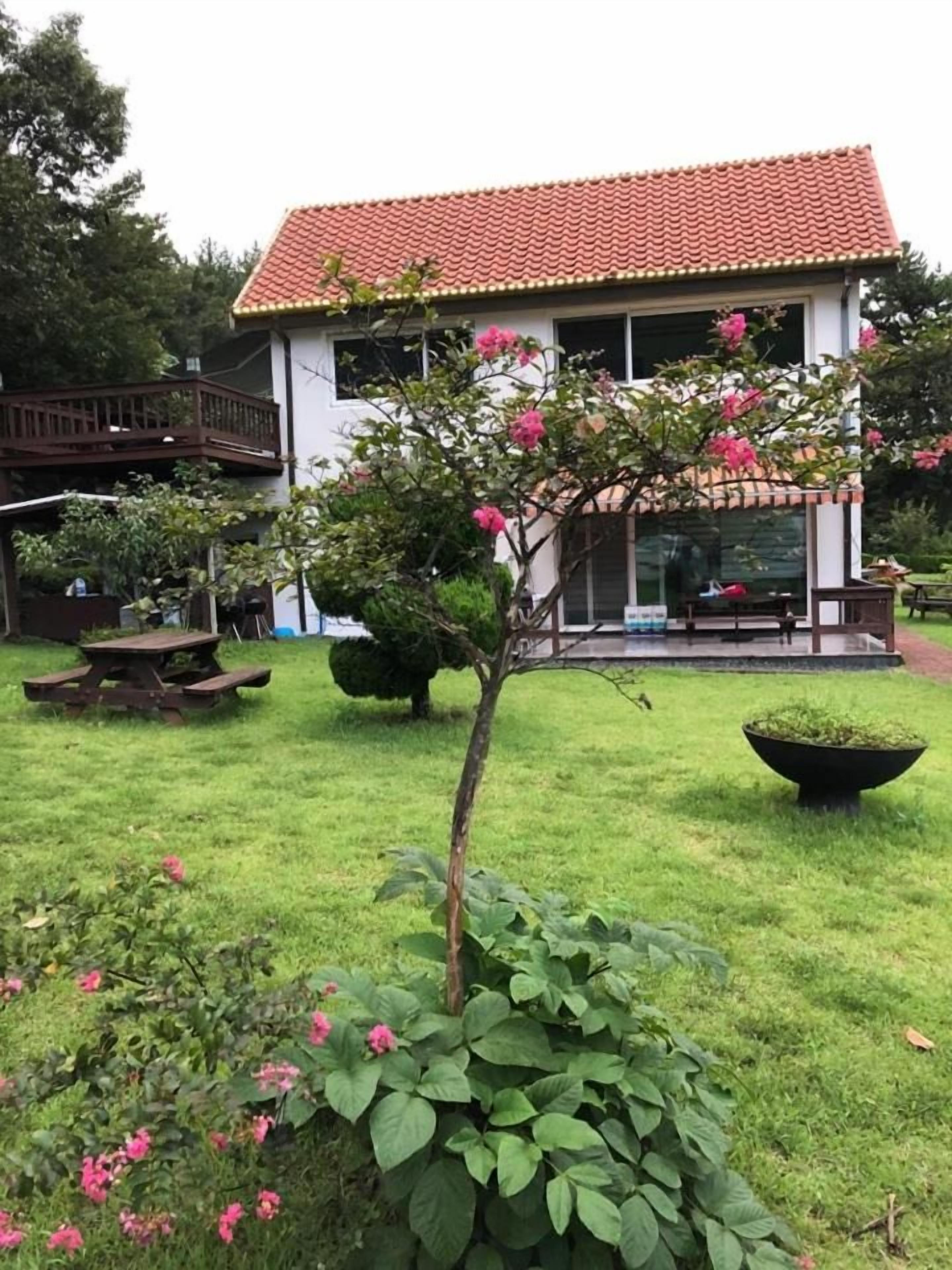 A house with a red-tiled roof, a deck, and a garden with pink flowers.