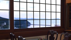 Un coin repas avec une table et des chaises, un vase de fleurs et une vue sur la mer par une fenêtre à carreaux.