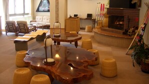 A spacious living room with a large wooden coffee table, comfortable seating, a fireplace, and a television mounted on the wall. - Hotel Khuls Shigakogen (Yamanouchi)