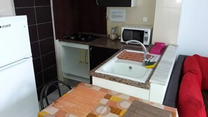 A compact kitchen with a refrigerator, stove, microwave, sink, and a small table with a mat. - Furnished Short Stay Apartment In Tunis (Tunis)