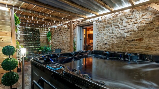 Un área de spa con jacuzzi, techo de madera, paredes de piedra y plantas en macetas.