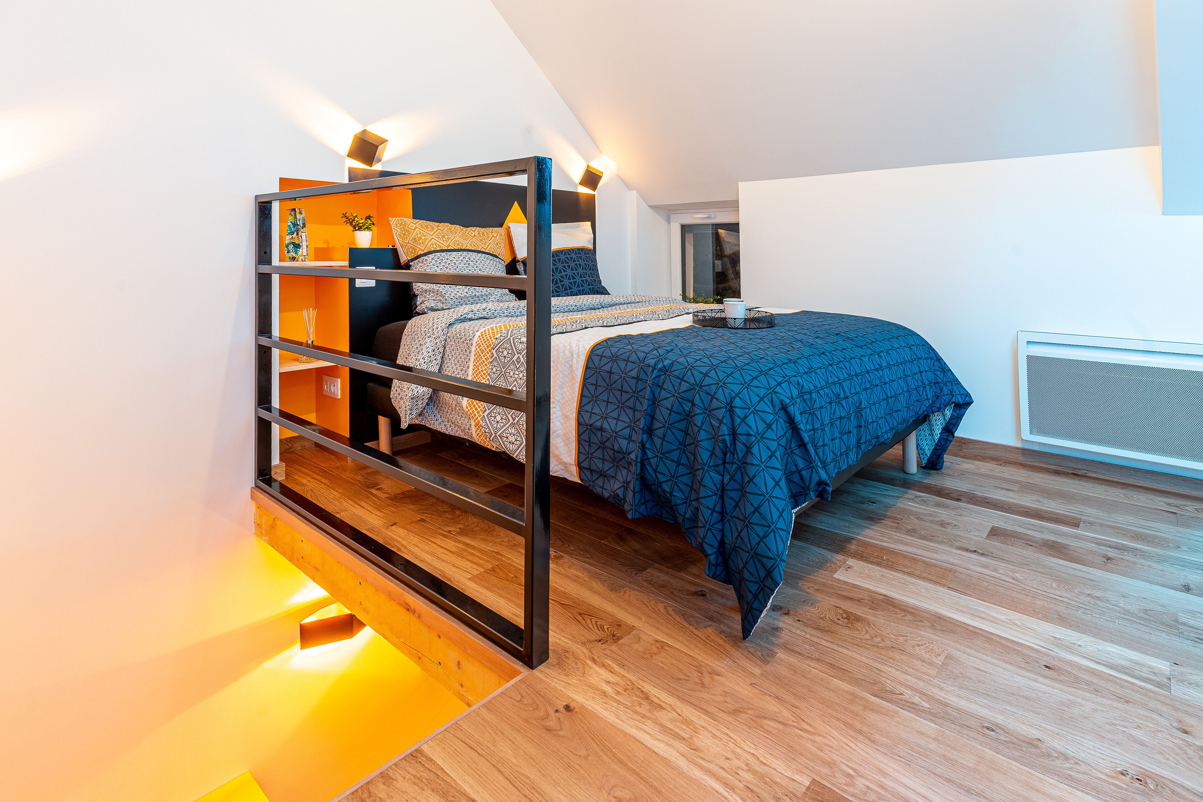 A bunk bed with a wooden frame, a blue patterned bedspread, and a bedside table with a lamp.