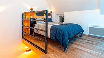 A bunk bed with a wooden frame, a blue patterned bedspread, and a bedside table with a lamp.
