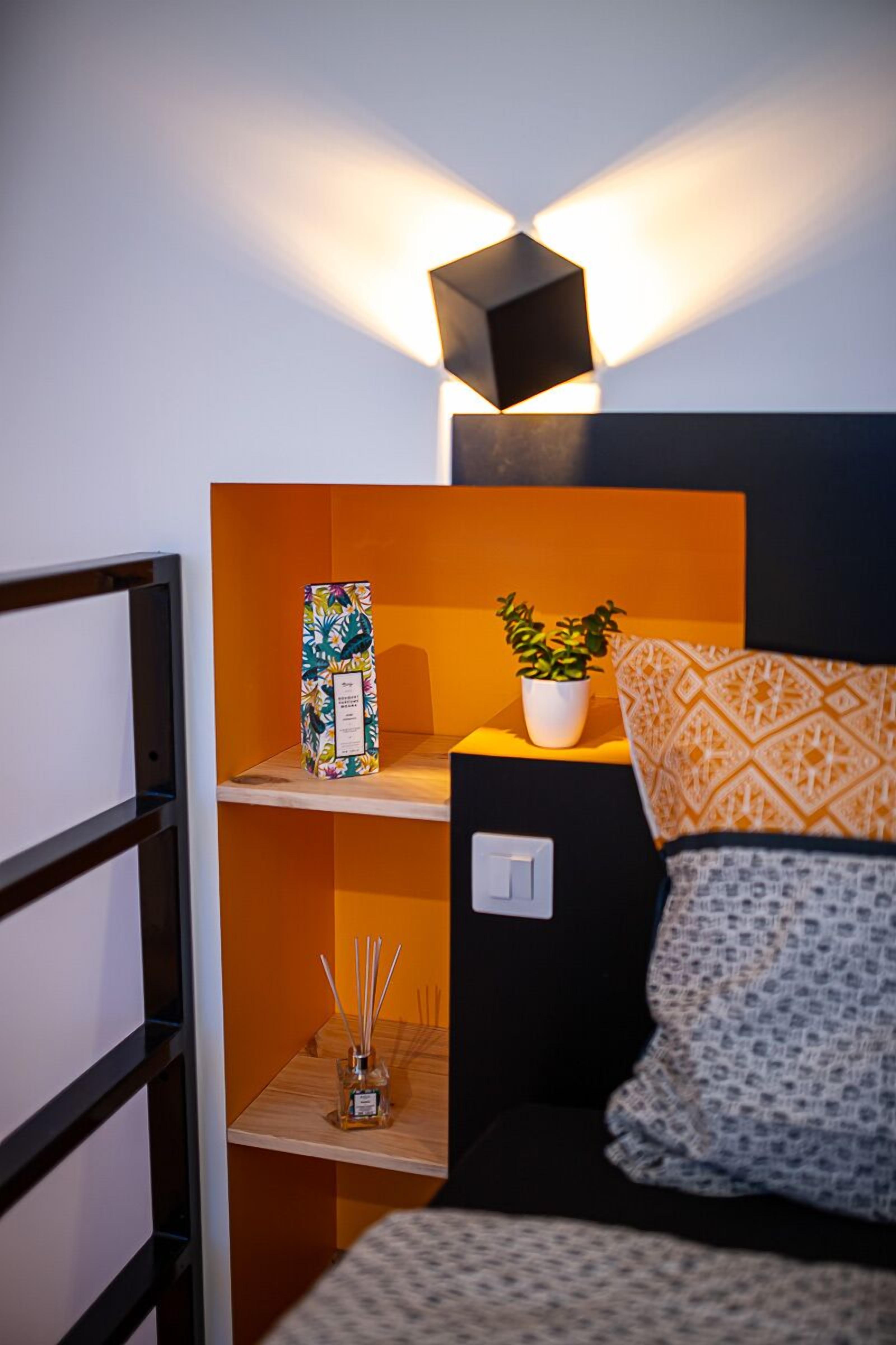Een gezellige kamer met een bed, een plankje met een plant erop en een wandlamp.