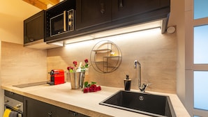 Una cocina moderna con un lavamanos negro, armarios de madera, un microondas integrado y una repisa circular con una vela.