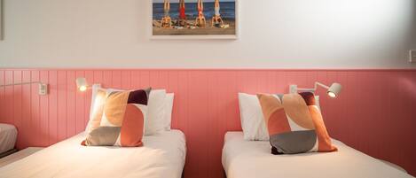 Habitación de hotel con dos camas, cabecero rosa y un cuadro con motivos playeros sobre las camas.