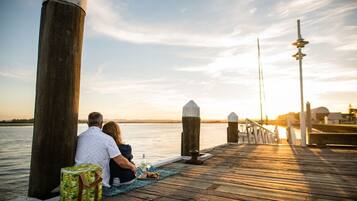 Una pareja sentada sobre un muelle de madera, con vista al agua y un atardecer de fondo.