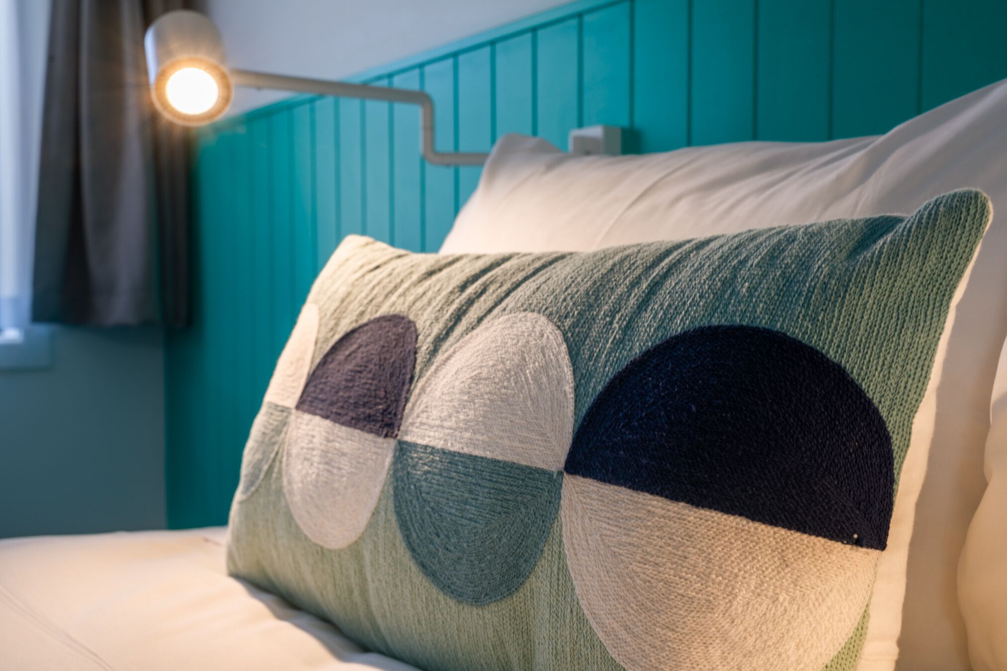 Un lit avec une tête de lit de couleur turquoise, un oreiller orné d’un motif circulaire et une lampe de chevet.