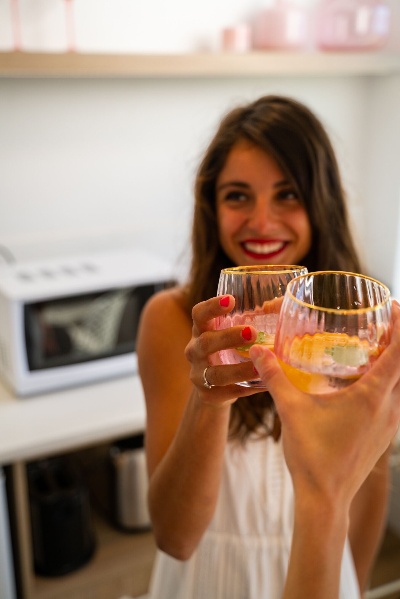 A person holding two glasses with a white appliance in the background.