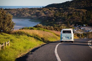 Una camioneta blanca circulando por una carretera sinuosa, con un paisaje costero de fondo.