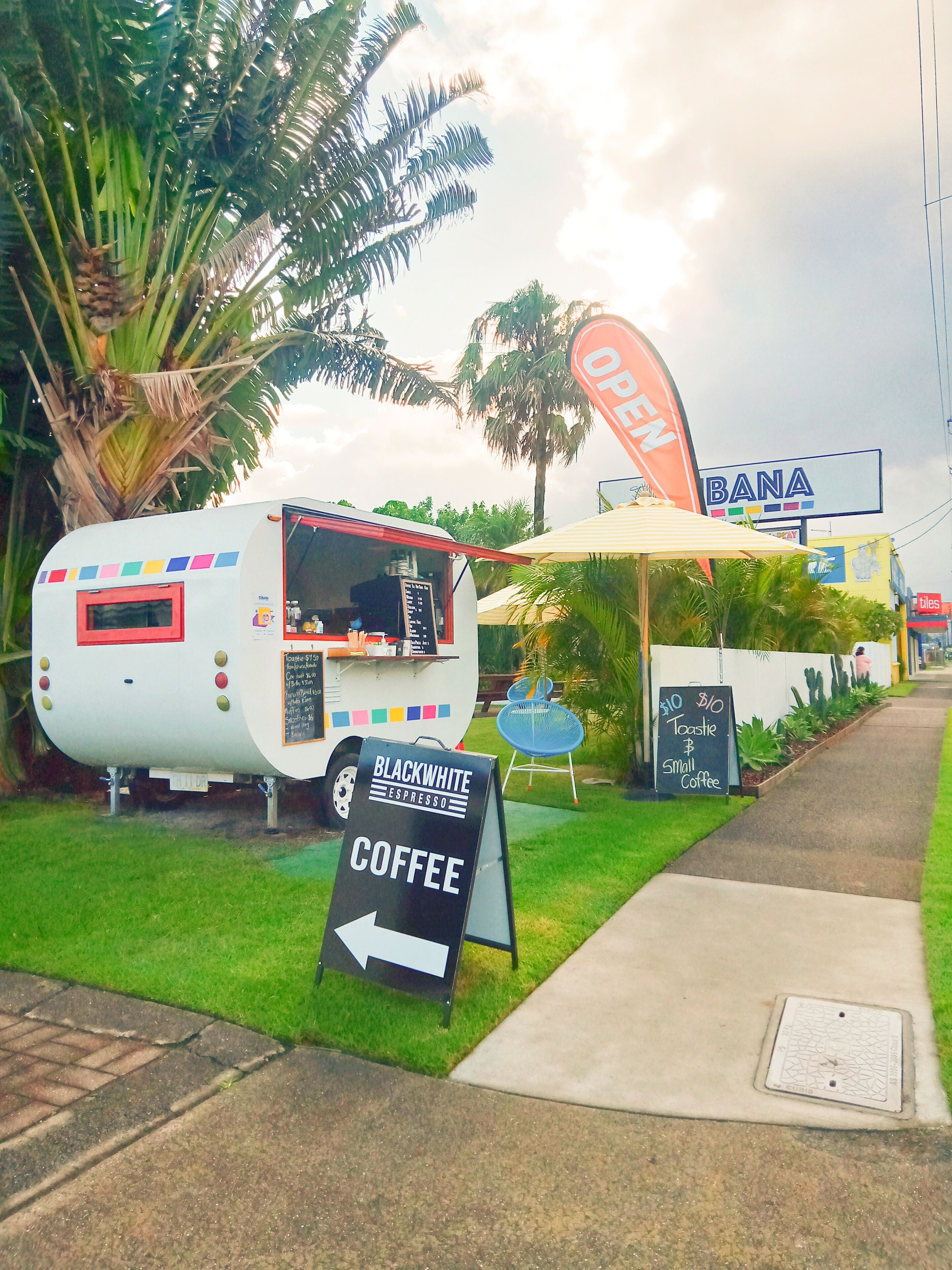 A food truck with a sign for Black & White Espresso Coffee, a 'BANA' sign, and a 'tiles' sign in the background.