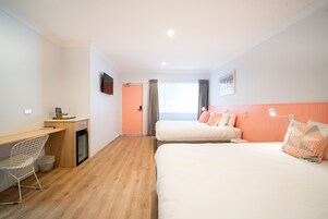 Habitación de hotel con dos camas, un escritorio, una silla y un televisor.