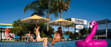 Una piscina con sillas de descanso y sombrillas, un flotador de flamenco y un letrero que dice 'The Cubana'.