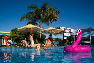 A swimming pool with lounge chairs and umbrellas, a flamingo float, and a sign for 'The Cubana'.