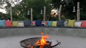 A concrete bench with colorful cushions and a fire pit in the center. - Jumbo Junction (Gunotsoga)