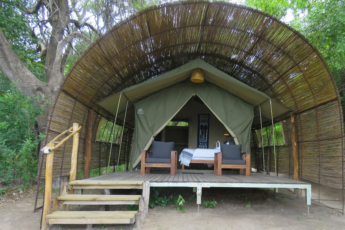 A tented accommodation with a wooden deck, two chairs, and a bed.