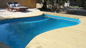 A swimming pool with a wooden deck, two lounge chairs, and a table. - Jumbo Junction (Gunotsoga)