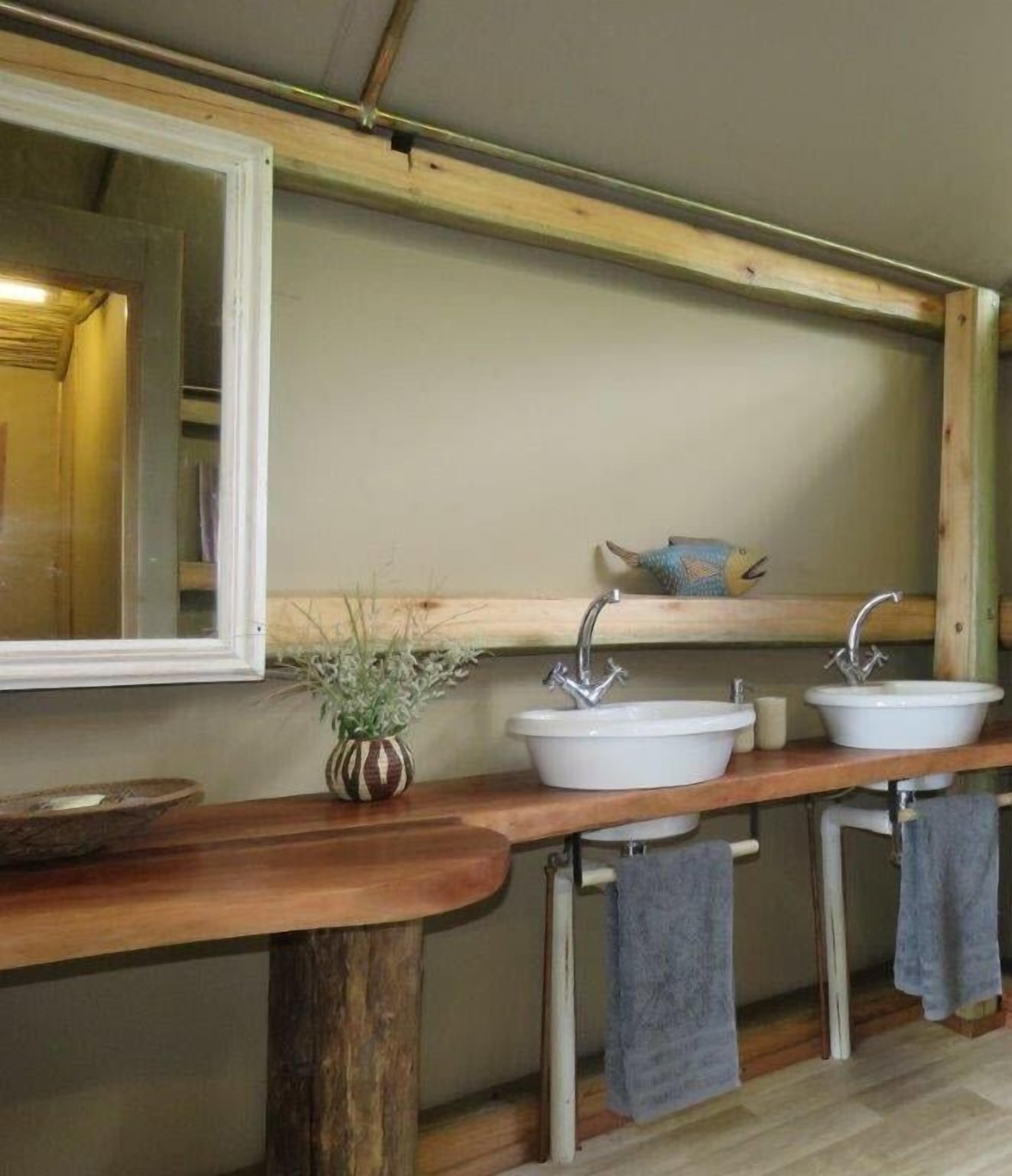 Un baño con tocador de madera, dos lavamanos, un espejo y una repisa con un objeto decorativo.