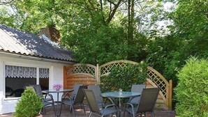 A patio with a table and chairs, surrounded by greenery and a wooden fence.