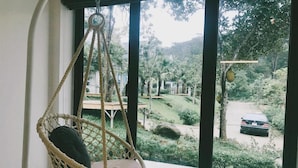 A room with a large window, a hanging chair, and a view of a garden and parked car outside.