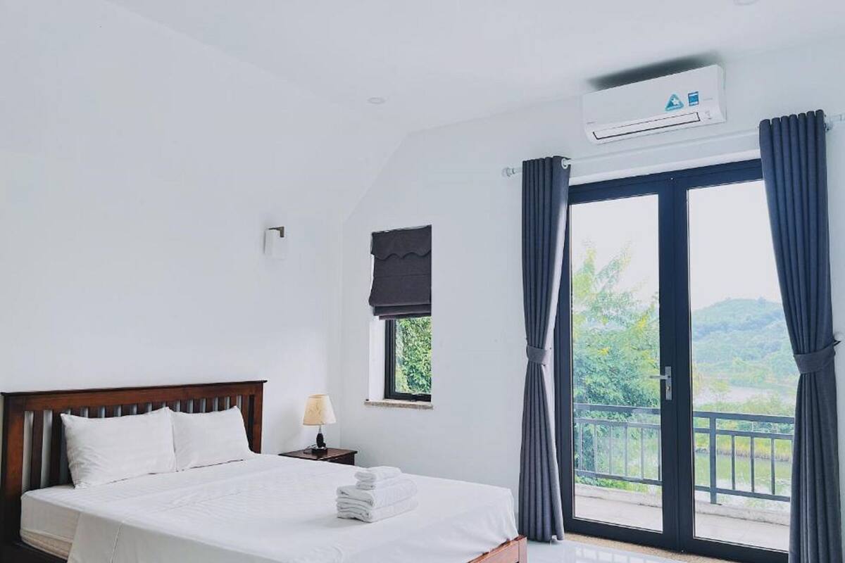 Un dormitorio con cama, mesita de noche, ventana con cortinas y aire acondicionado.