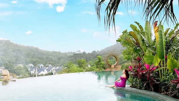 A woman sitting by a pool with a view of houses and greenery.