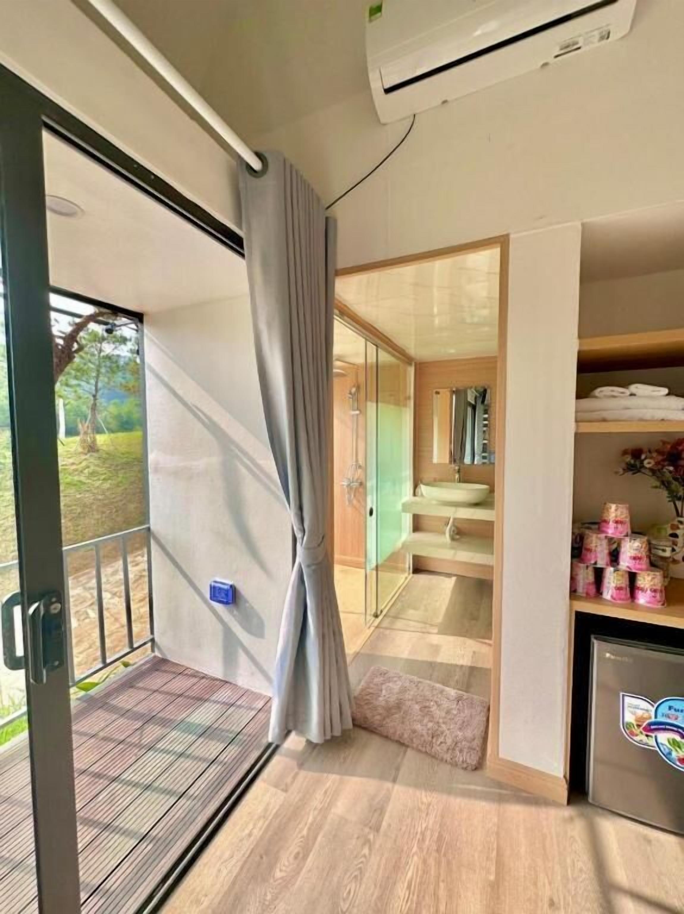 A modern bathroom with a glass shower, a sink, and a toilet. There is a curtain partially drawn, and a small rug on the floor.