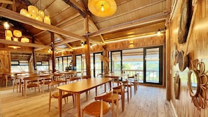 A spacious wooden dining area with high ceilings and large windows offering a view of the outdoors.