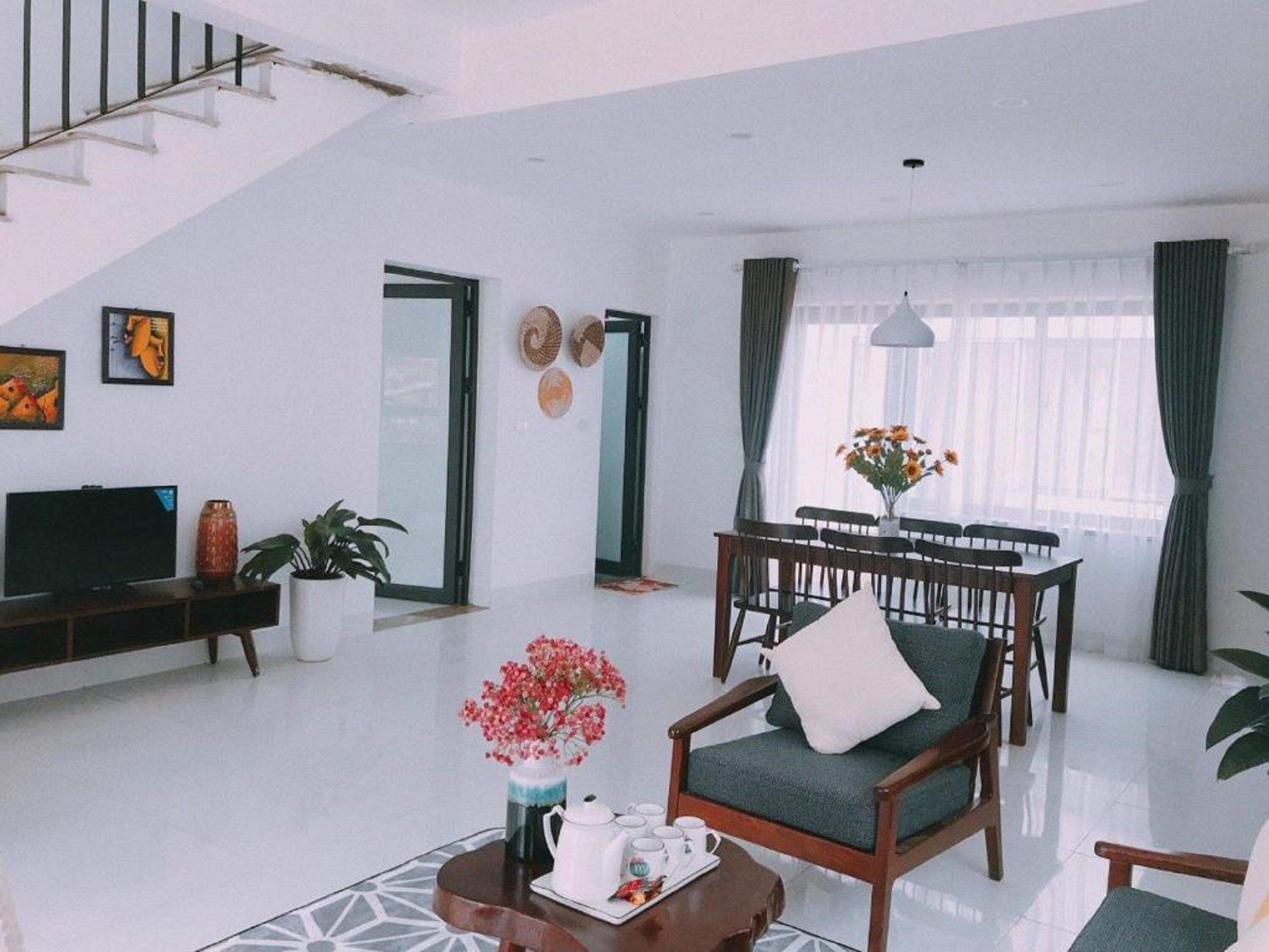 A modern living room with a staircase, a dining area, and a TV on a stand.