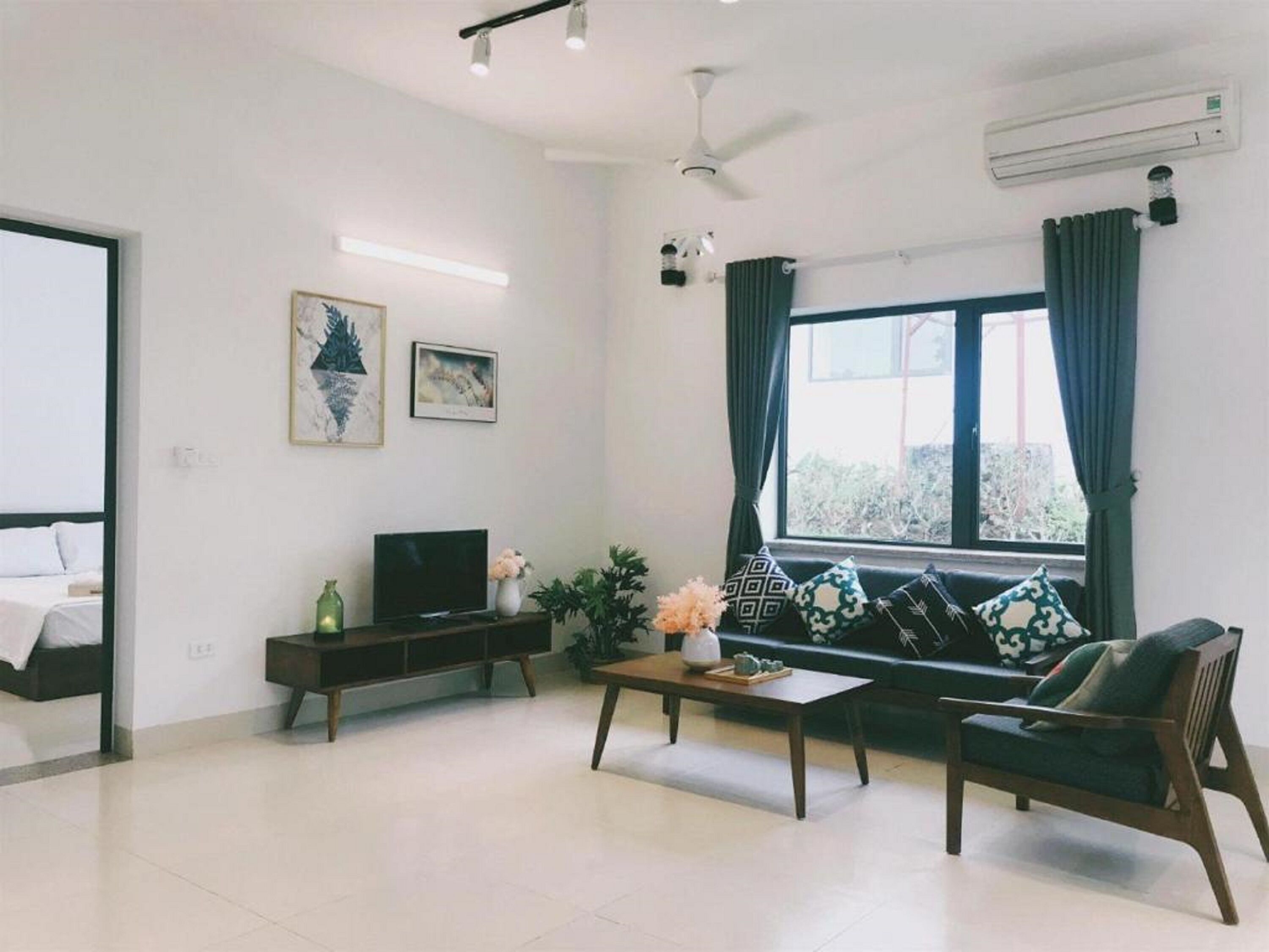 A modern living room with a sofa, a coffee table, a TV on a stand, a ceiling fan, and an air conditioning unit.
