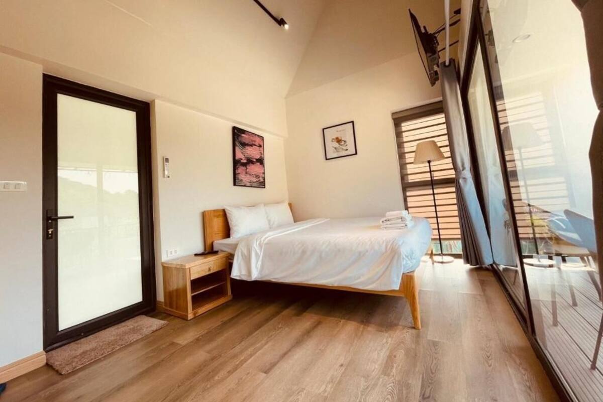 Un dormitorio con una cama, una mesita de noche de madera, una puerta y una ventana con persianas.