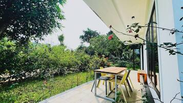 Um pátio com mesa e cadeiras, cercado por vegetação exuberante e um edifício branco.