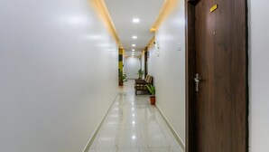 A hallway with a wooden door on the right, a bench with chairs, and potted plants. - Zenith Residency (Bengaluru)