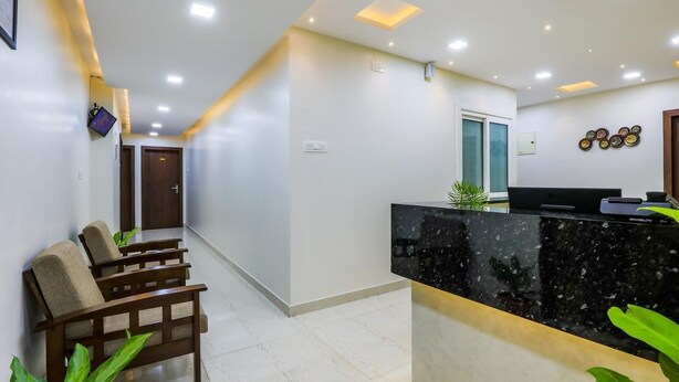 A reception area with a black marble counter, wooden chairs, and a plant. - Zenith Residency (Bengaluru)