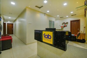Taulell de recepció amb un cartell de 'fab hotels', una porta de fusta, un ventilador i un escriptori amb un ordinador i un vas de flors.