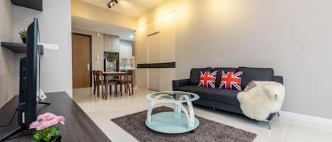 Una sala de estar moderna con una televisión de pantalla plana, una mesa de centro de vidrio, un sofá con almohadones decorativos y una pequeña planta en maceta.