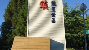 Ein hohes, vertikales Schild mit chinesischen Schriftzeichen, an einer Metallkonstruktion befestigt, mit einer Holzplattform davor.