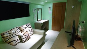 Ein Zimmer mit einer Couch, einem Schreibtisch, einem Spiegel, einem Fernseher und einer Tür.