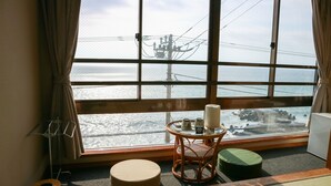A room with a large window, a wicker chair, a small table with a candle, and a round ottoman. - Hotel & Resort Izunone (Higashiizu)