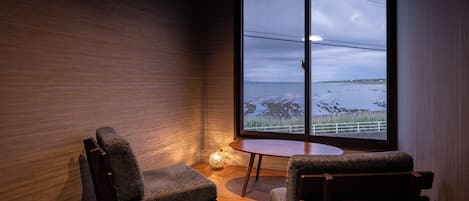 Una habitación con un amplio ventanal, dos sillas, una mesita y una lámpara.