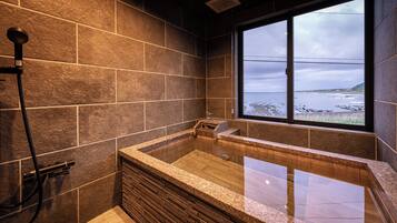 A modern bathroom with a large bathtub, a shower, and a view of the ocean through a large window.