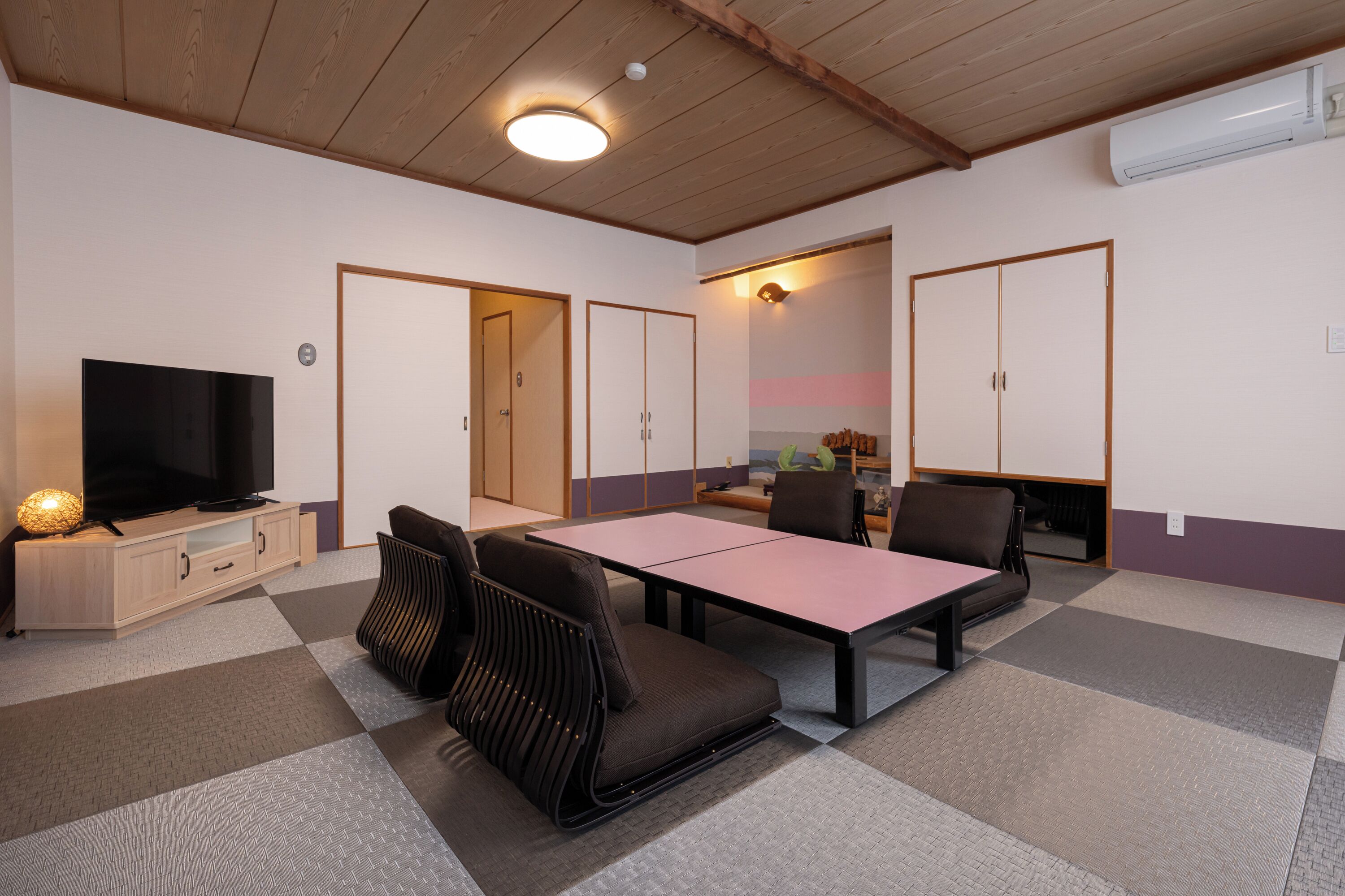 A room with a television, a dining table, and chairs. There are cabinets and a ceiling fan.