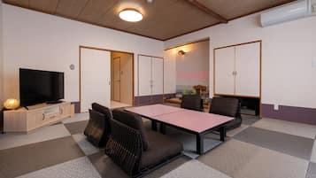 A room with a television, a dining table, and chairs. There are cabinets and a ceiling fan.